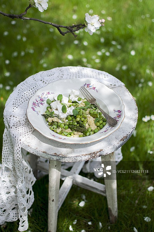 小米沙拉配芦笋，豌豆，山羊奶酪和新鲜薄荷放在旧的花园椅子上图片素材