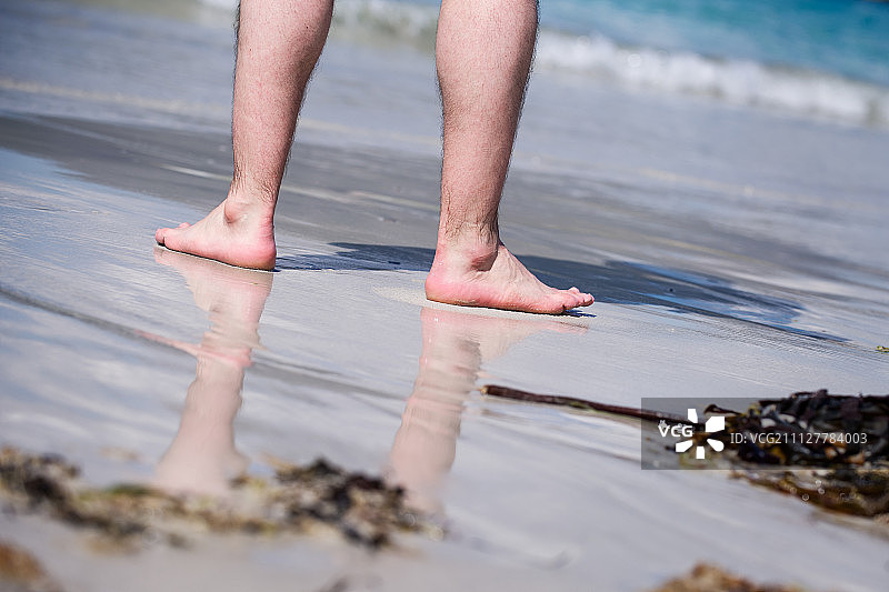 男光脚在温暖的沙滩上，男人在阳光明媚的海滩上散步与绿松石水在…图片素材