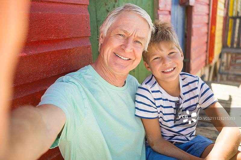 快乐的男孩和祖父坐在海滩的墙上的肖像图片素材