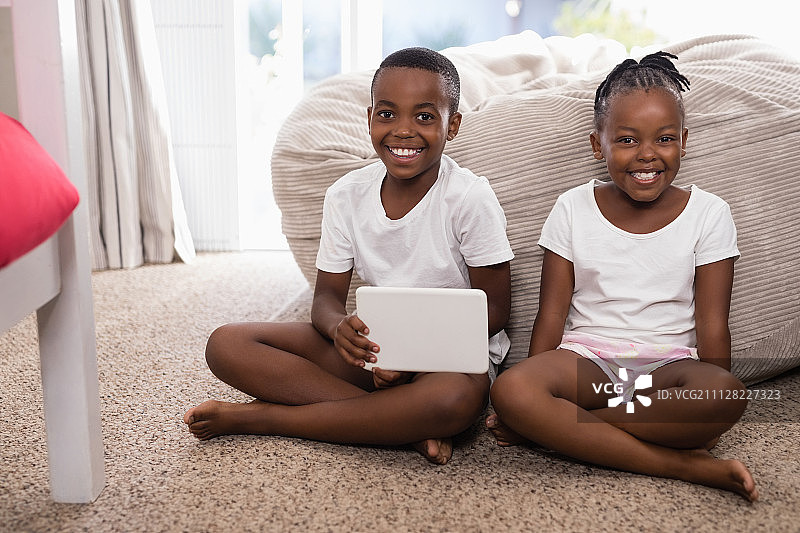 快乐的兄弟姐妹们坐在地毯上，拿着平板电脑图片素材