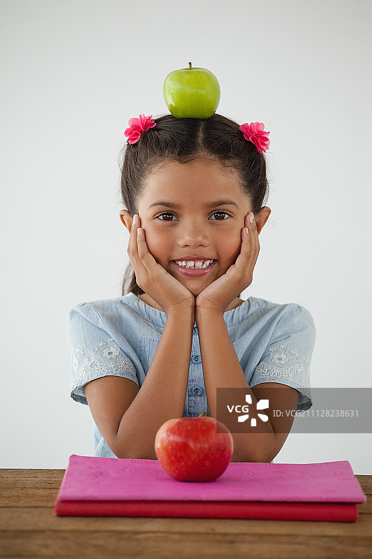 一名女学生的肖像，坐在绿色的苹果在她的头对白色的背景图片素材