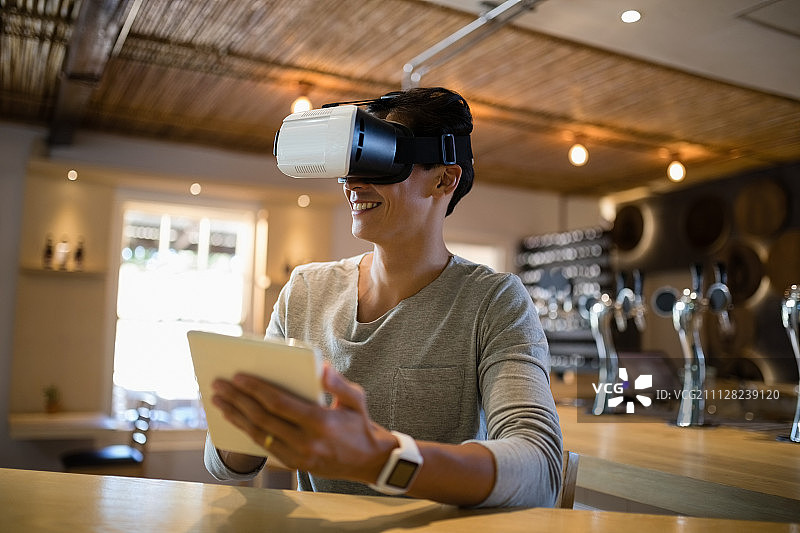 微笑的男人使用虚拟现实耳机和数字平板电脑在餐厅图片素材