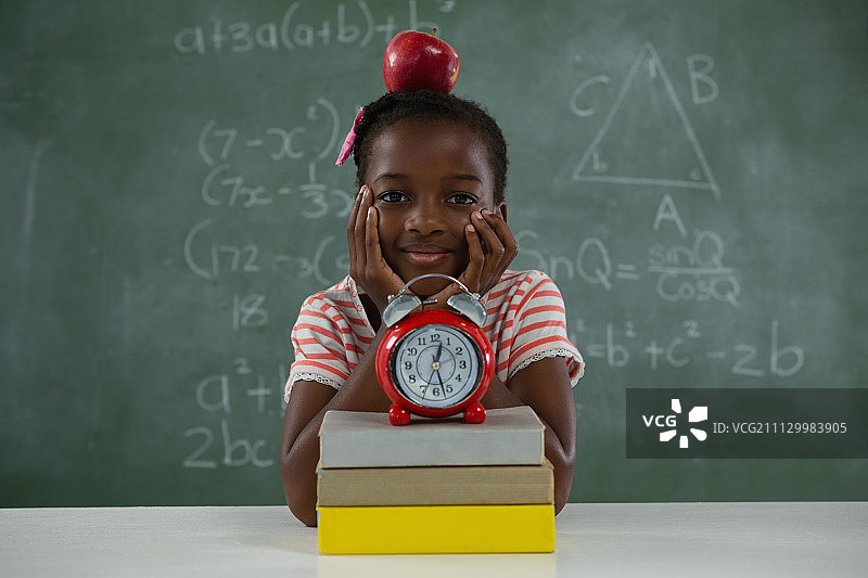 一名女学生坐在黑板前，头上戴着红苹果图片素材