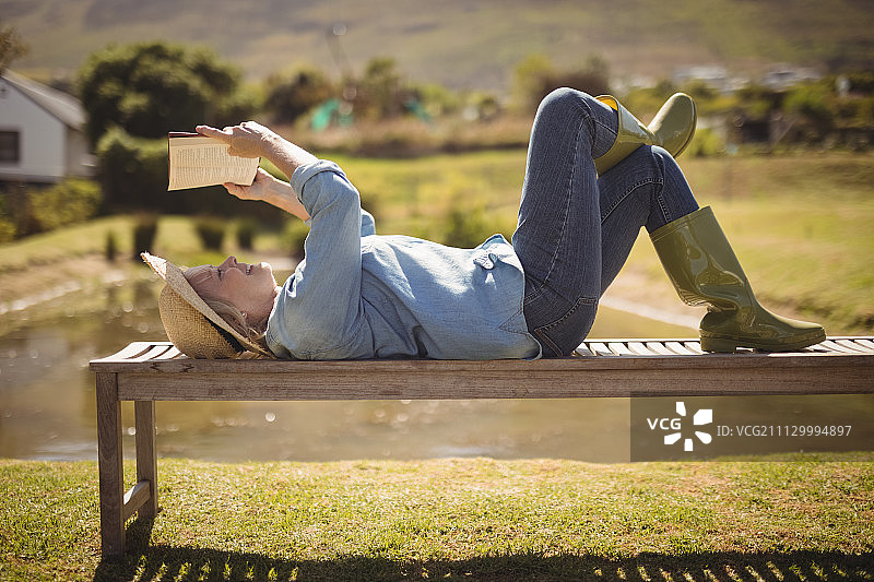 一位老妇人在一个阳光明媚的日子躺在公园的长椅上看书图片素材