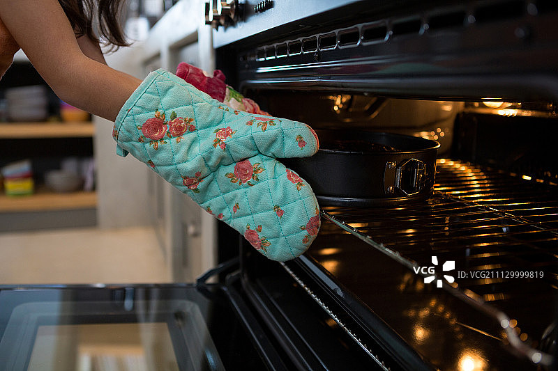在厨房的烤箱里，戴着手套的女孩把蛋糕和容器放在了手图片素材
