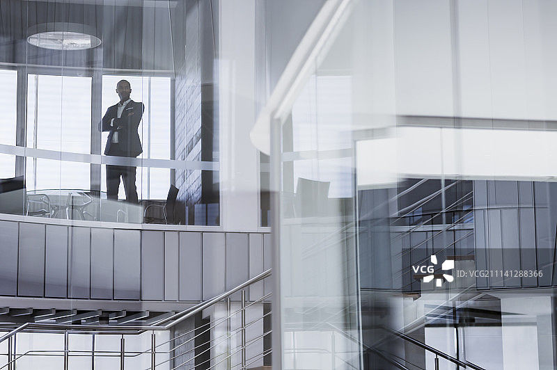 自信的CEO商人双臂交叉站在现代办公室的窗户前图片素材