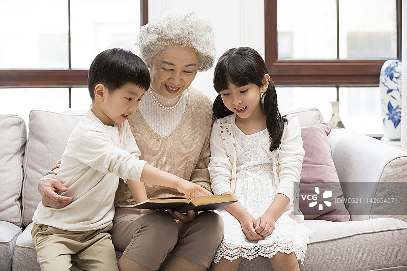 开心的奶奶和孙子孙女在沙发上看书图片素材