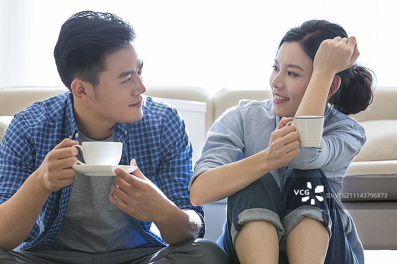 年轻情侣坐在客厅地上喝咖啡休息图片素材