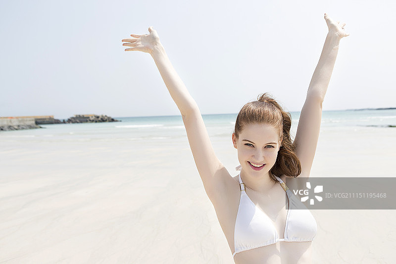 身穿白色比基尼的女子站在沙滩上，双手高举图片素材