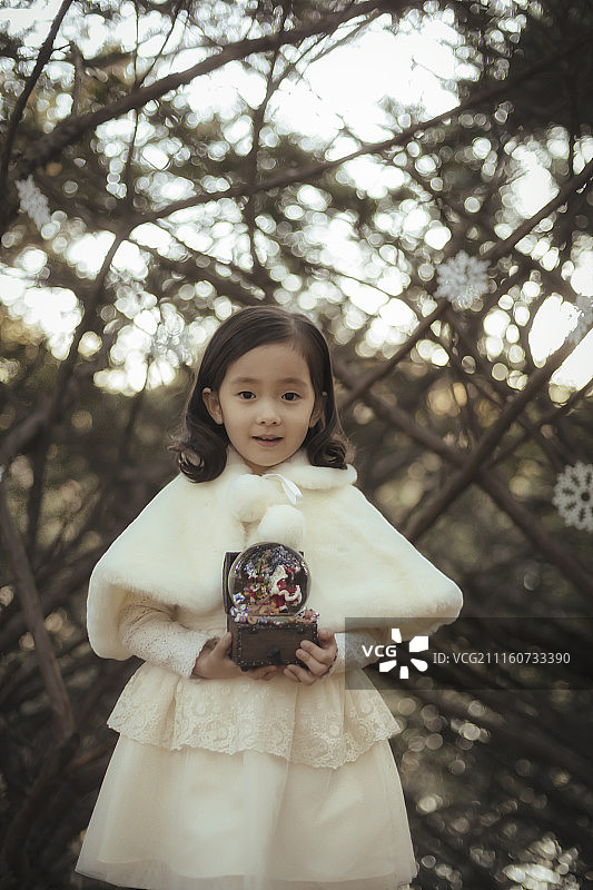 小女孩站在街道上的树木中，拿着冬天的装饰图片素材