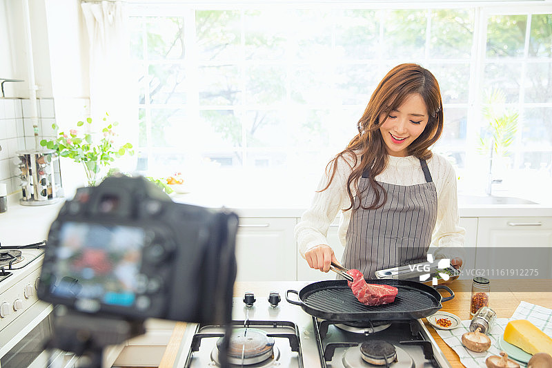 韩国人，女人，厨房，烹饪，牛肉(红肉)，烤(烹饪)，厨师，食物造型师，微笑，相机，拍摄，1人图片素材