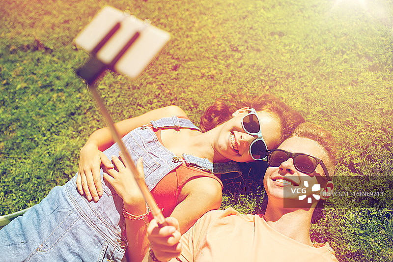 爱和人的概念——快乐的青少年情侣在夏天戴着太阳镜躺在草地上，用智能手机自拍。一对幸福的情侣在夏天用智能手机自拍图片素材
