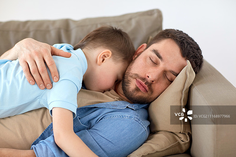 家庭、童年、父亲、休闲和人的概念——幸福的父亲和儿子睡在家里的沙发上。快乐的父子俩睡在家里的沙发上图片素材