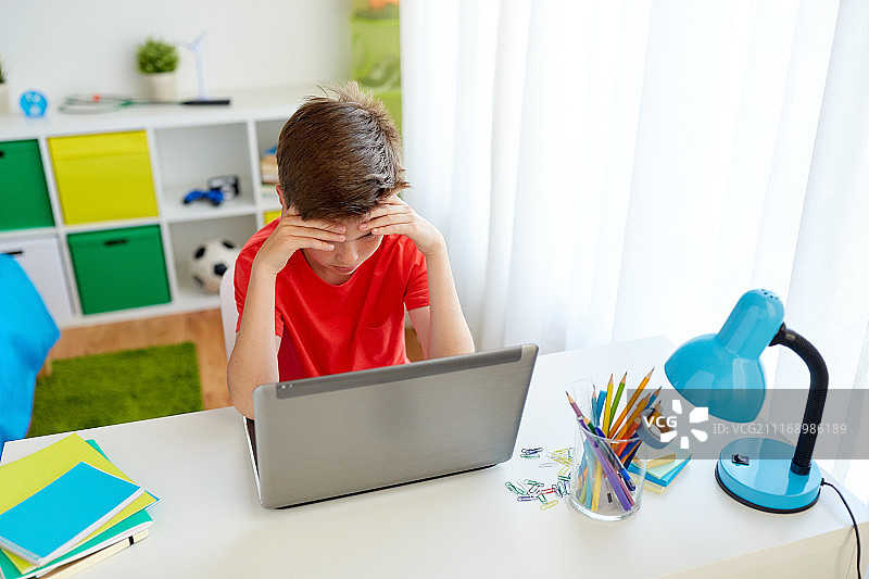 教育、网络欺凌和人们的概念——可悲的学生男孩在家里用笔记本电脑遭受欺凌。疲惫的学生男孩在家里用笔记本电脑图片素材
