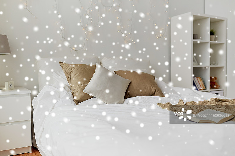 舒适的家，室内和假日概念-舒适的卧室与床和圣诞花环灯在雪。卧室里有床和圣诞花环图片素材