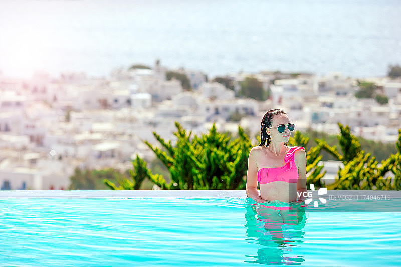 年轻美丽的女人在室外豪华游泳池享受暑假图片素材
