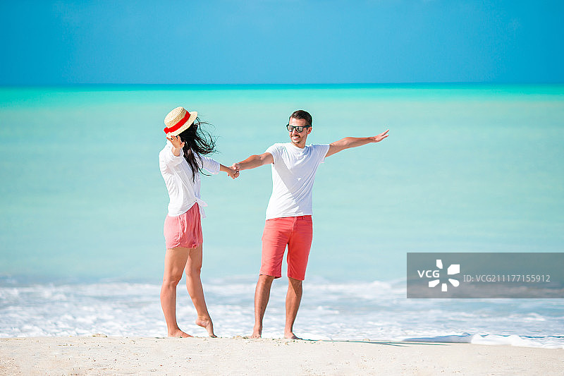 一对年轻夫妇在白色沙滩和绿松石海水的热带海滩上散步图片素材