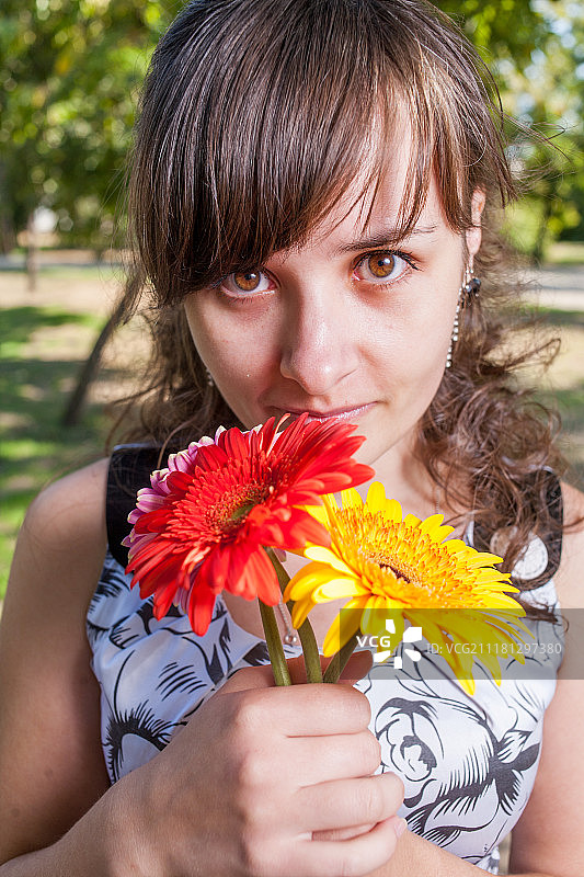 一个可爱的女人用三朵花看着相机的肖像。图片素材