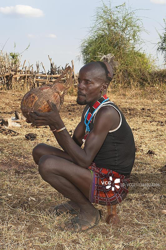 非洲埃塞俄比亚南部奥莫河谷，一名哈马尔男子在葫芦里喝高粱啤酒图片素材