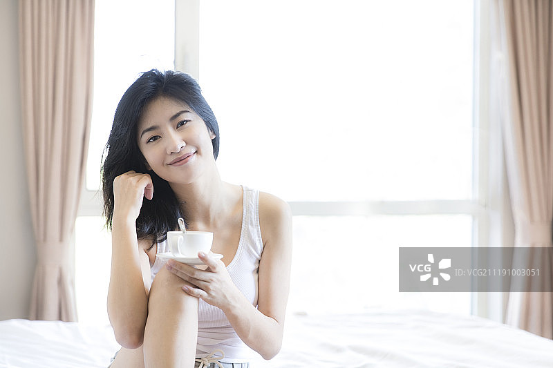 年轻女子坐在卧室床上喝咖啡图片素材