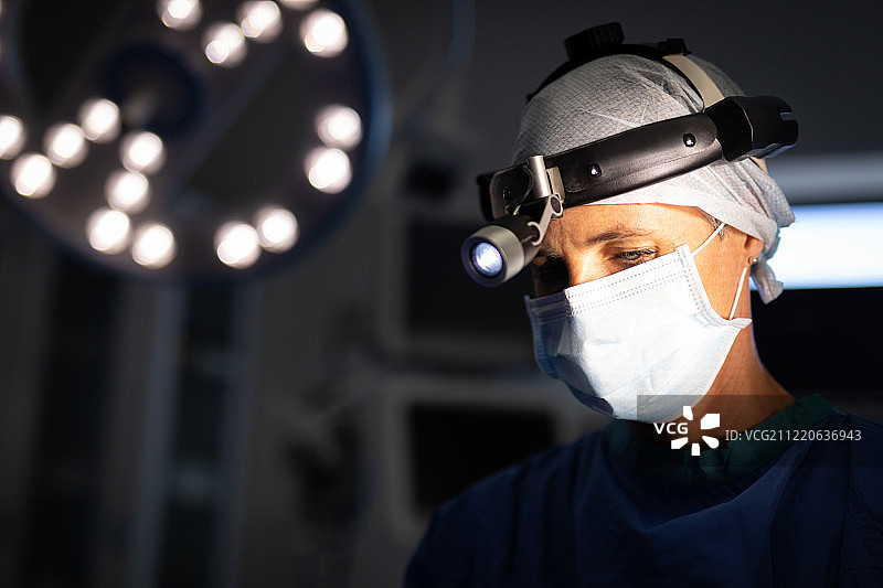 一个成熟的白人女性外科医生的正面视图戴着外科头灯在手术室操作。图片素材
