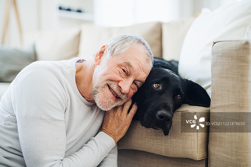 一个快乐的老人在家里和宠物狗玩。图片素材