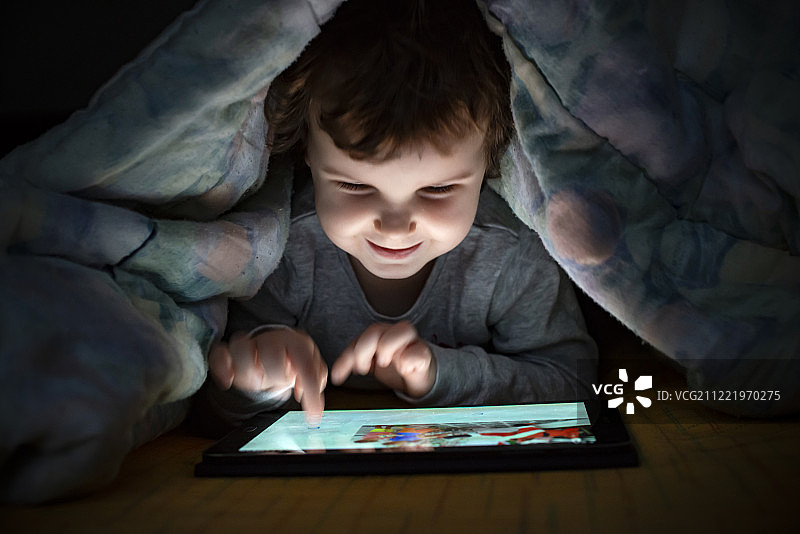 小女孩躺在床上看她的平板电脑。照亮孩子足总图片素材