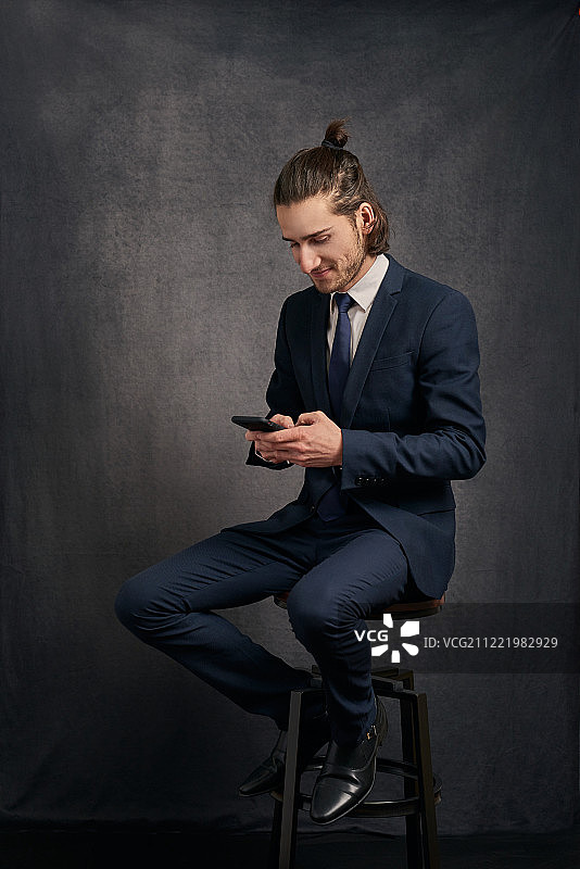 穿着西装的时髦男人，坐在酒吧的凳子上发短信图片素材