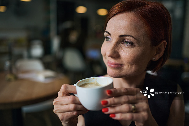 一个女人坐在咖啡馆里，拿着一杯咖啡的肖像。图片素材