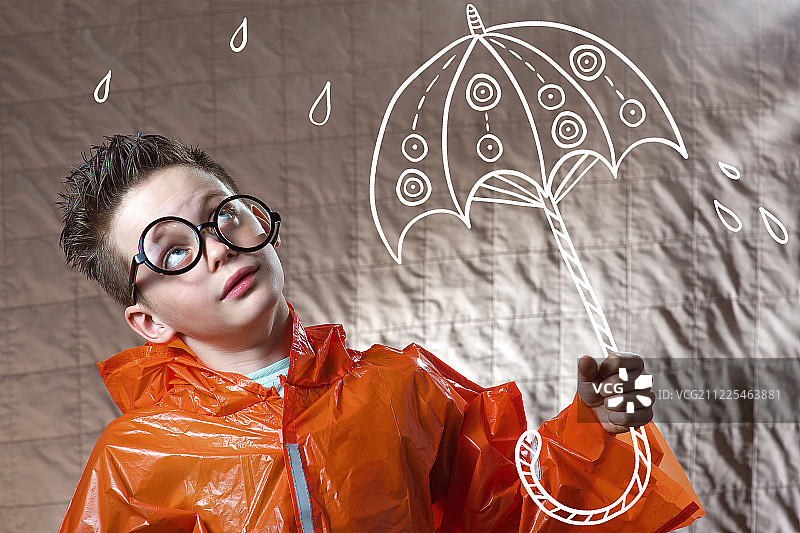 一个男孩穿着橙色雨衣，拿着一把彩伞站在雨中图片素材