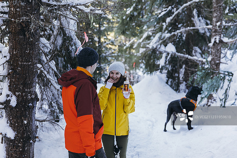 一对夫妇和一只狗在冬天的森林里和一个女人展示智能手机，惠斯勒，不列颠哥伦比亚省，加拿大图片素材