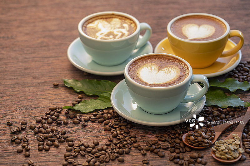 三杯含有漂亮拉花的拿铁咖啡和不同烘焙程度的咖啡豆图片素材