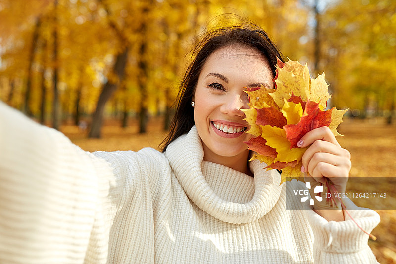 季节和人的概念-快乐的年轻女子与枫叶在秋天的公园自拍。女人与树叶在秋天的公园自拍图片素材