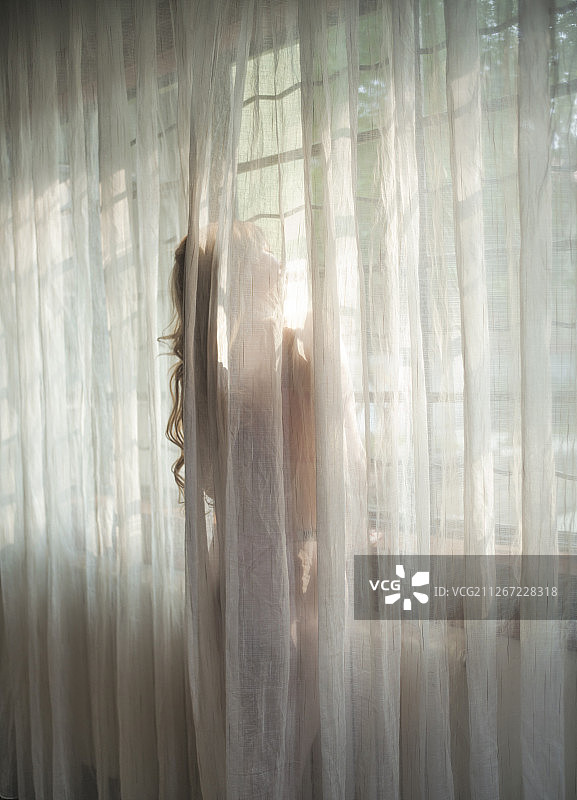 窗帘下被光笼罩的少女图片素材