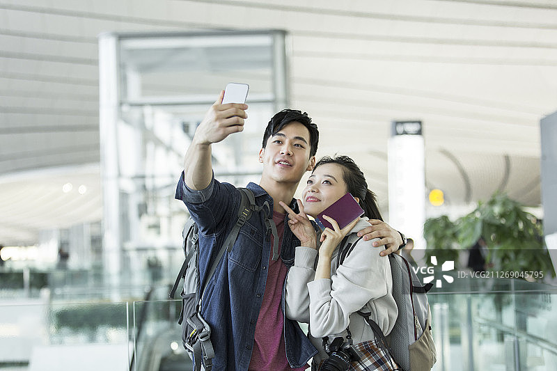 快乐情侣在机场拿着护照和机票使用手机自拍图片素材