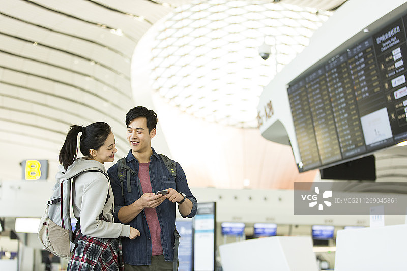 青年情侣使用手机在机场核对飞机航班信息图片素材