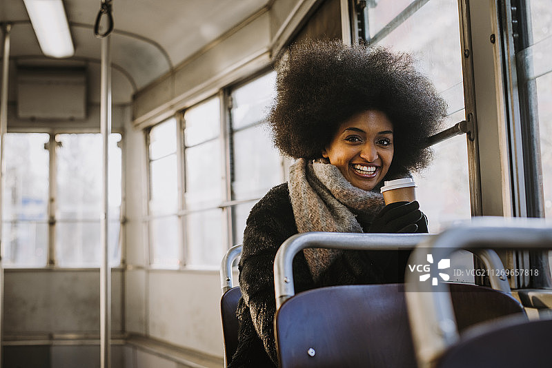 一幅年轻女子的肖像，留着非洲式发型，在公共交通工具上喝着咖啡图片素材