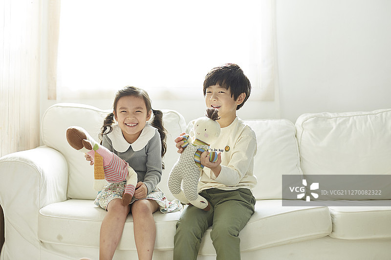 小女孩和小男孩坐在室内沙发上玩洋娃娃图片素材