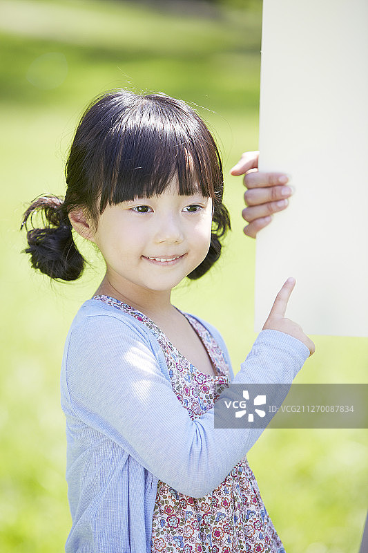 小女孩在公园里指着白色空白横幅的照片图片素材