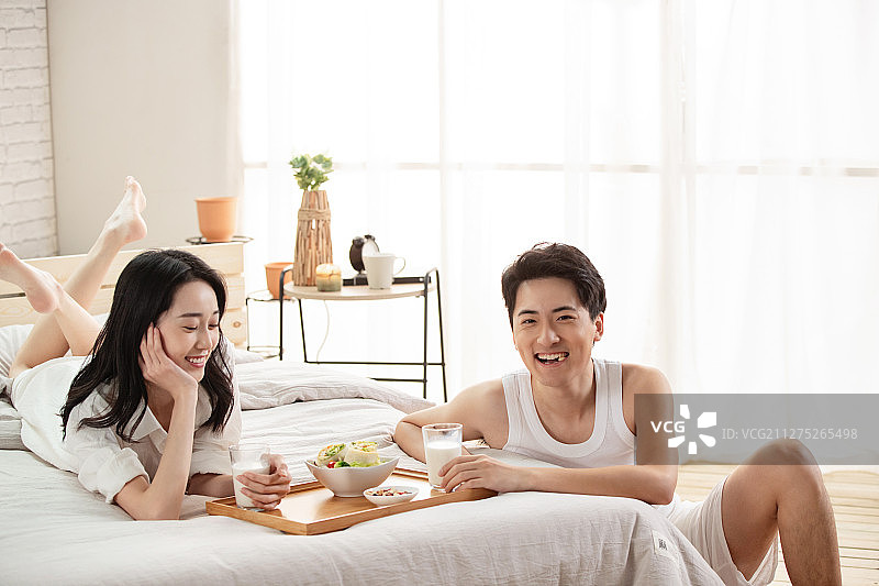 快乐的年轻情侣在床上吃早餐图片素材