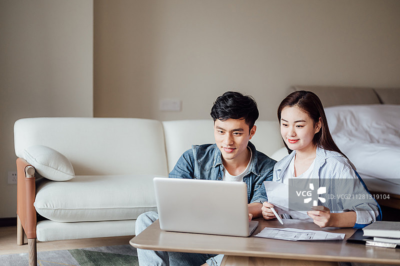 亚洲年轻情侣在家使用电脑看户型图图片素材