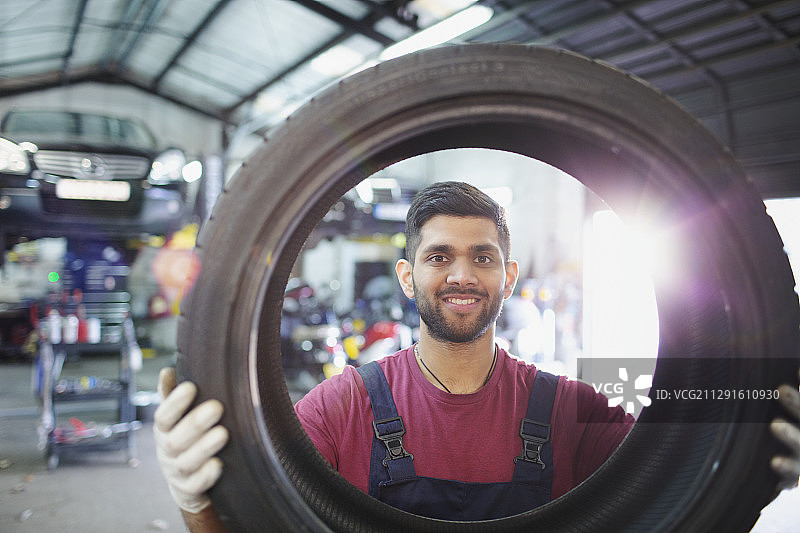 肖像自信，微笑的男性技工在汽车修理店持有轮胎图片素材