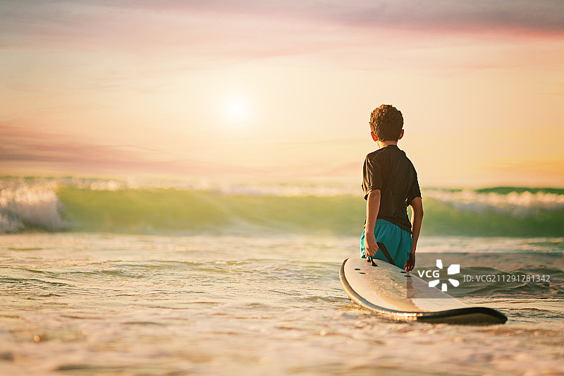一个冲浪男孩抱着冲浪板看海浪的背影图片素材