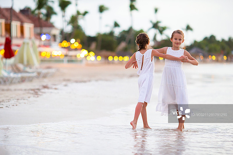 两个穿着白色裙子的小女孩在沙滩上的水里跳舞图片素材