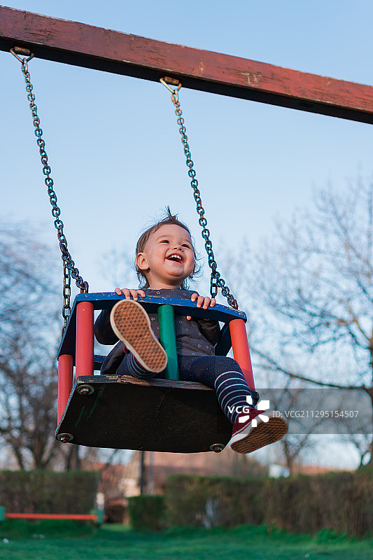 塞尔维亚，苏博蒂卡，一个快乐的小孩坐在户外儿童游乐场的秋千上图片素材