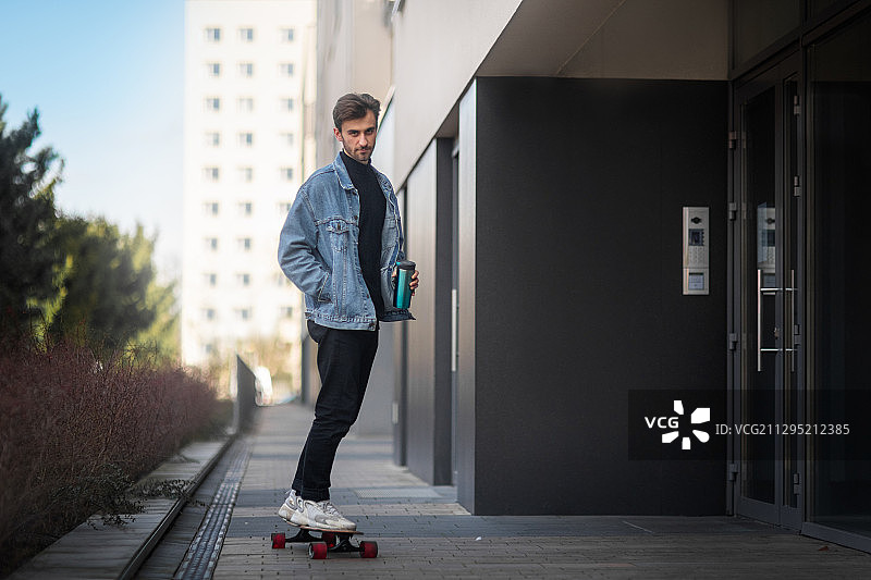 波兰克拉科夫，一名男子拿着旅行杯在人行道上玩滑板图片素材