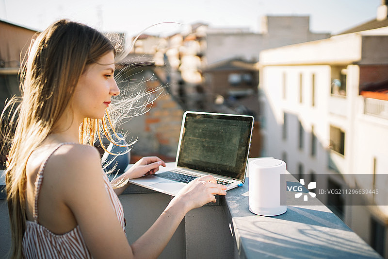 西班牙莱莱达，一名年轻女子在屋顶露台上使用笔记本电脑图片素材