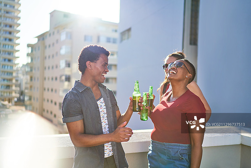 快乐的年轻朋友们在阳光明媚的城市屋顶阳台上喝啤酒图片素材
