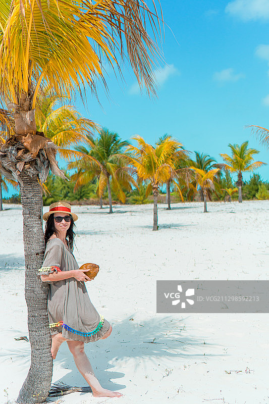 在热带海滩上，一名女子靠着棕榈树站立图片素材