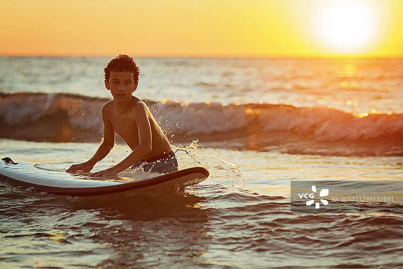 男孩冲浪者准备骑在美丽的日落光的海浪上图片素材
